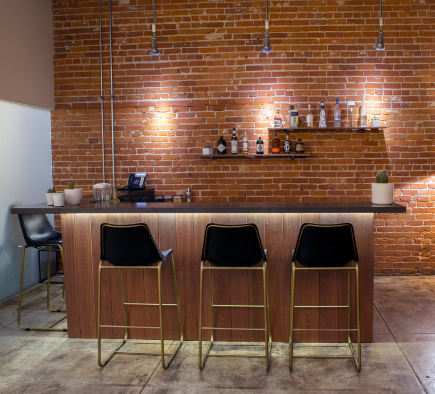 Cette photo montre un bar de salon industriel en L de taille moyenne avec des tabourets, un placard sans porte, un plan de travail en surface solide, une crédence rouge, une crédence en brique, sol en béton ciré et un sol gris.