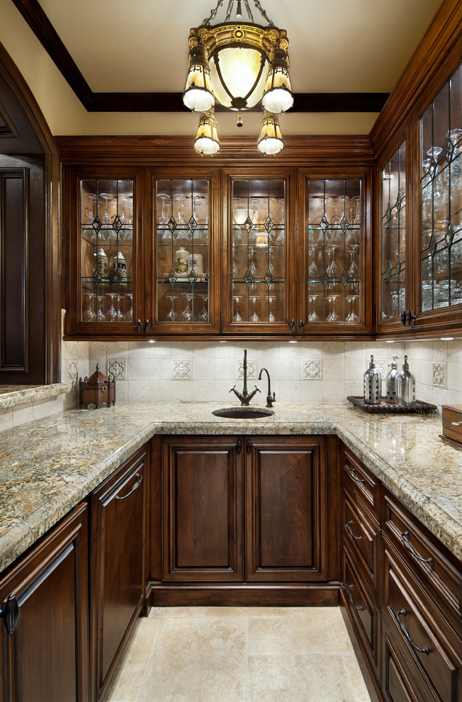 This is an example of a classic u-shaped home bar in Houston with a submerged sink, glass-front cabinets, dark wood cabinets, beige splashback and beige floors.