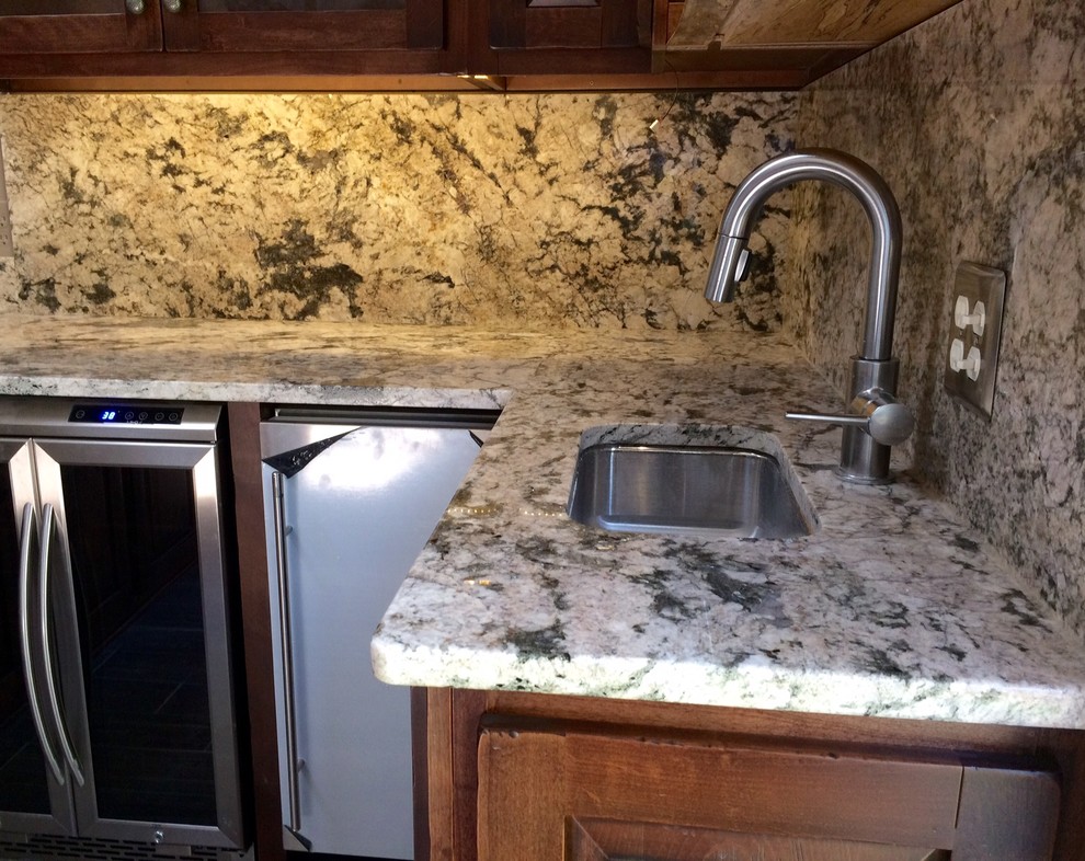 Imagen de bar en casa con barra de bar en U rural de tamaño medio con fregadero bajoencimera, armarios estilo shaker, puertas de armario de madera en tonos medios, encimera de granito y salpicadero de losas de piedra