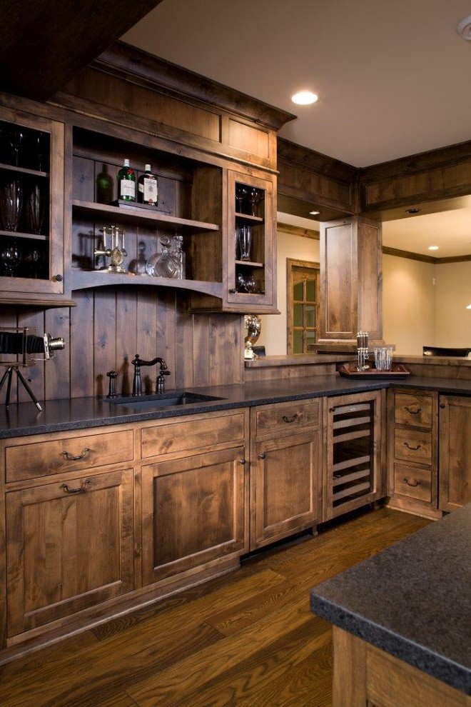 Ejemplo de bar en casa en U de estilo americano con suelo de madera oscura, fregadero bajoencimera, armarios estilo shaker y puertas de armario de madera en tonos medios