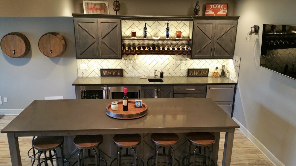 Ejemplo de bar en casa con barra de bar lineal rústico grande con fregadero bajoencimera, armarios estilo shaker, puertas de armario de madera en tonos medios, encimera de acrílico, salpicadero blanco, salpicadero de azulejos tipo metro, suelo marrón, encimeras marrones y suelo vinílico