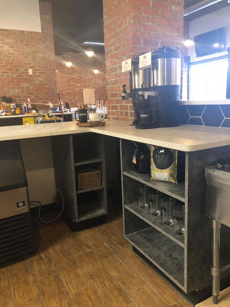 This is an example of a large industrial l-shaped breakfast bar in Omaha with a built-in sink, open cabinets, grey cabinets, onyx worktops, black splashback, ceramic splashback, ceramic flooring, brown floors and white worktops.