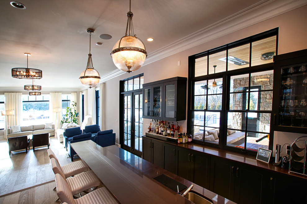 Example of a large transitional galley medium tone wood floor and brown floor seated home bar design in New York with an undermount sink, glass-front cabinets, blue cabinets and black countertops