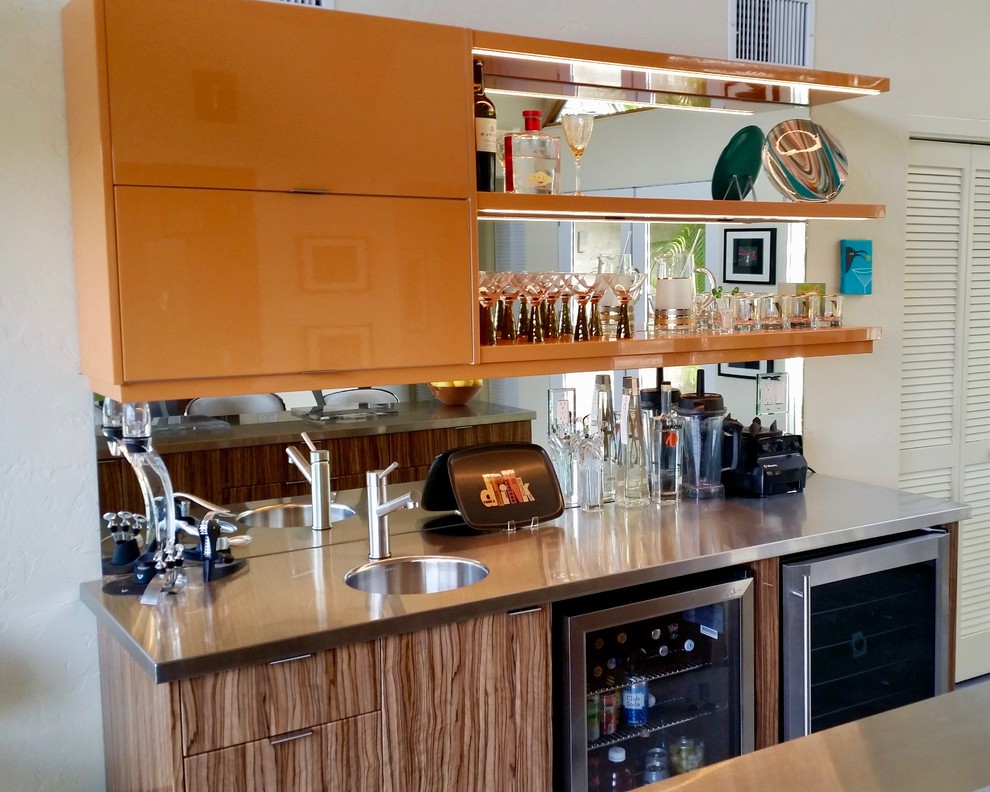 Modelo de bar en casa con fregadero lineal vintage de tamaño medio con fregadero integrado, armarios con paneles lisos, puertas de armario naranjas, encimera de acero inoxidable y salpicadero con efecto espejo