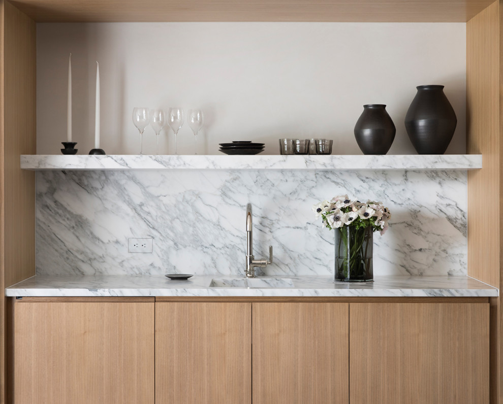 Cette image montre un petit bar de salon minimaliste en bois clair avec un évier encastré, plan de travail en marbre, une crédence blanche, une crédence en dalle de pierre et un plan de travail blanc.