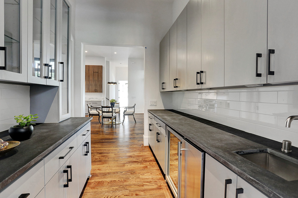 Exempel på en mellanstor modern svarta parallell svart hemmabar med vask, med en undermonterad diskho, släta luckor, grå skåp, marmorbänkskiva, vitt stänkskydd, stänkskydd i cementkakel, mellanmörkt trägolv och brunt golv
