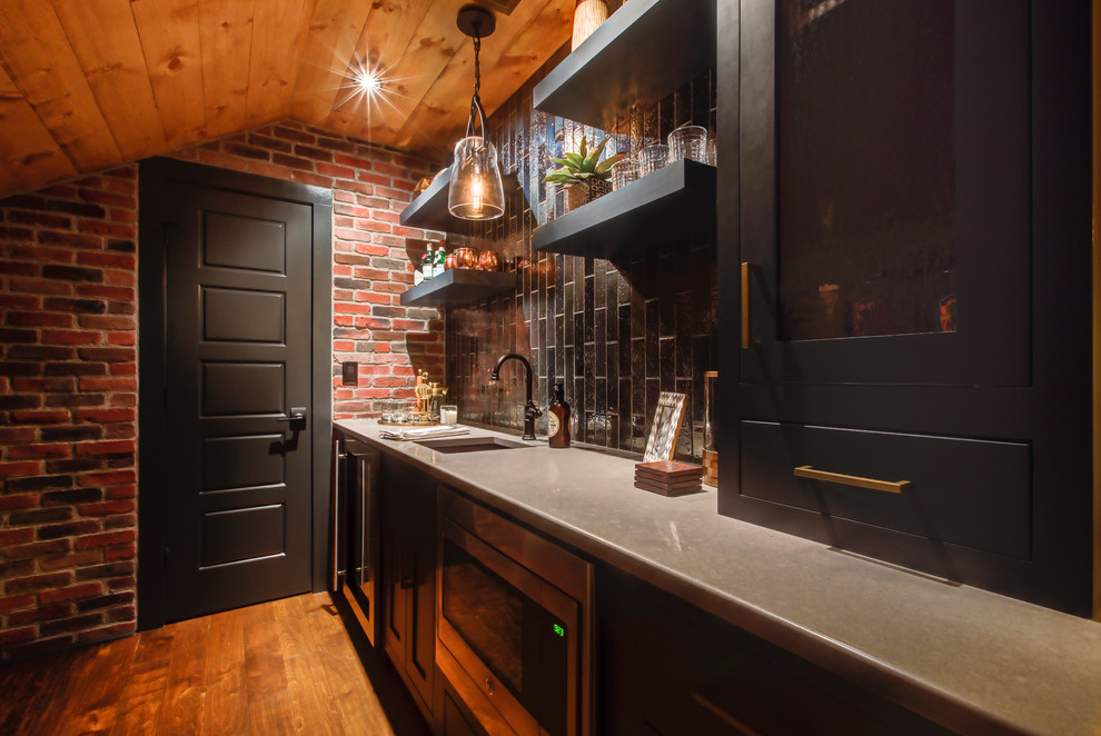 Photo of a medium sized industrial single-wall wet bar in Raleigh with a submerged sink, recessed-panel cabinets, black cabinets, engineered stone countertops, black splashback, glass tiled splashback, dark hardwood flooring and brown floors.