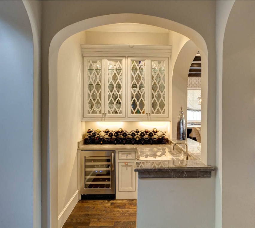 Idéer för att renovera en mellanstor vintage l-formad hemmabar med vask, med luckor med glaspanel, vita skåp, marmorbänkskiva, mörkt trägolv och brunt golv