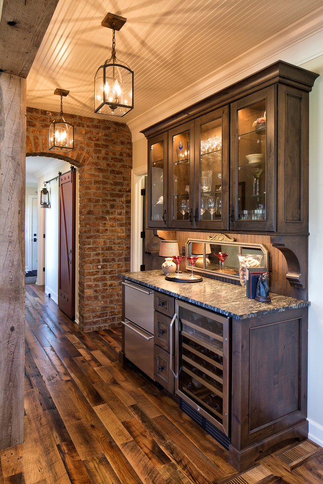 Example of a mid-sized farmhouse single-wall medium tone wood floor wet bar design in Minneapolis with no sink, recessed-panel cabinets, dark wood cabinets, granite countertops and brown backsplash