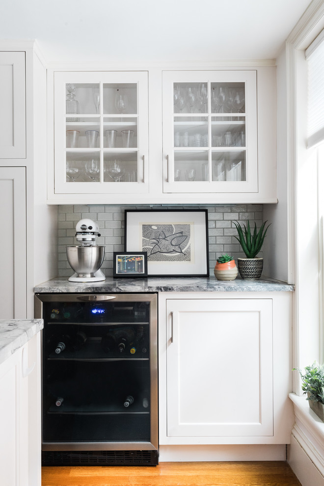 Inspiration for a transitional medium tone wood floor home bar remodel in Boston with glass-front cabinets, white cabinets, white backsplash, subway tile backsplash and multicolored countertops