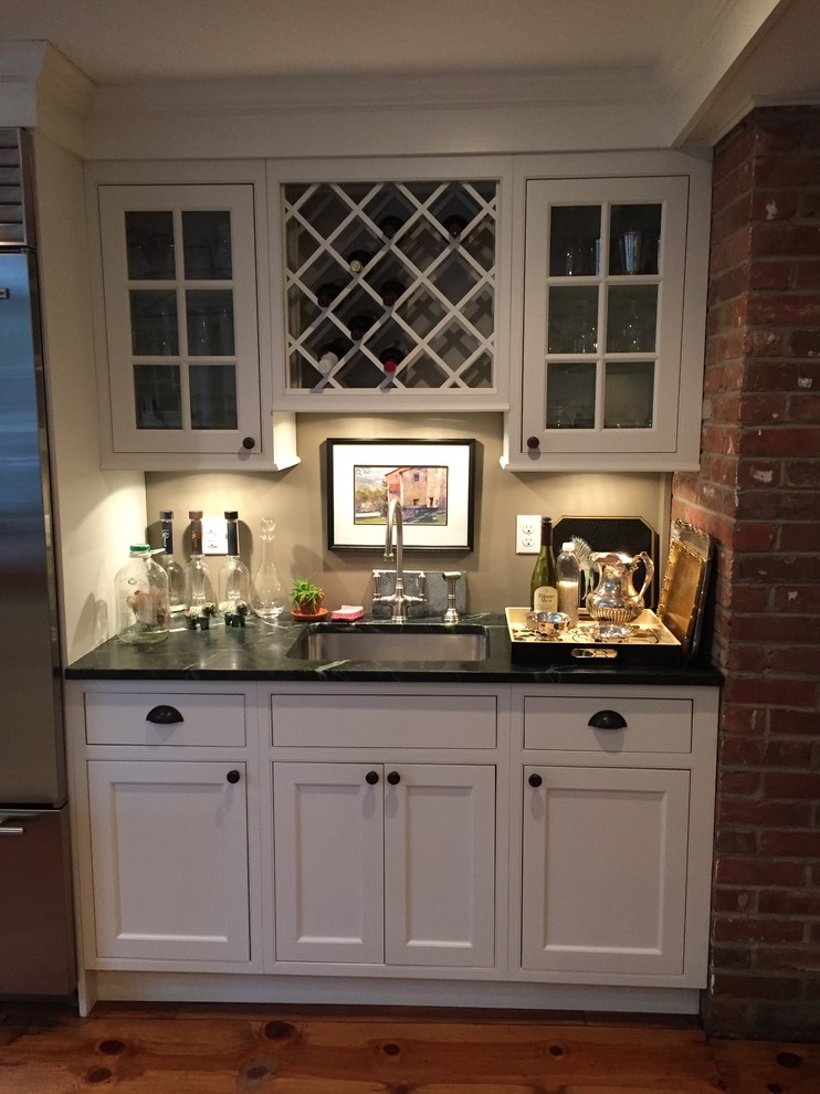 Photo of a small country single-wall wet bar in New York with a submerged sink, shaker cabinets, white cabinets, beige splashback, medium hardwood flooring and brown floors.