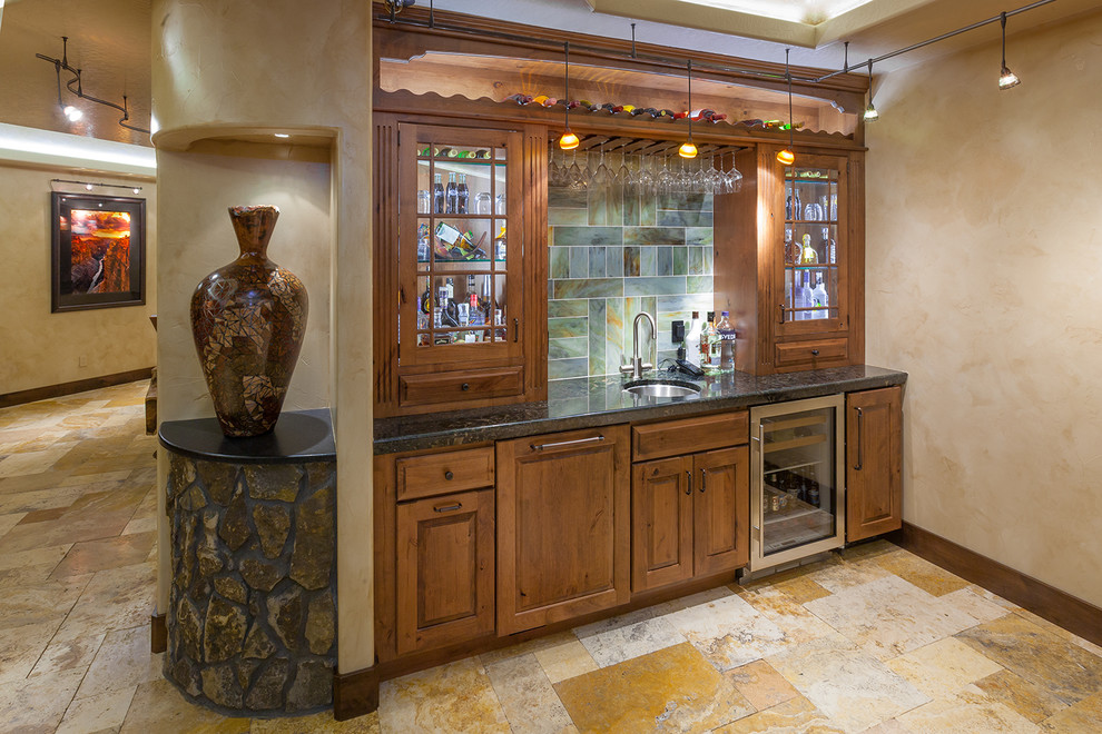 Inspiration for a medium sized rustic single-wall wet bar in Denver with a submerged sink, glass-front cabinets, dark wood cabinets, granite worktops, multi-coloured splashback, stone tiled splashback, travertine flooring and beige floors.
