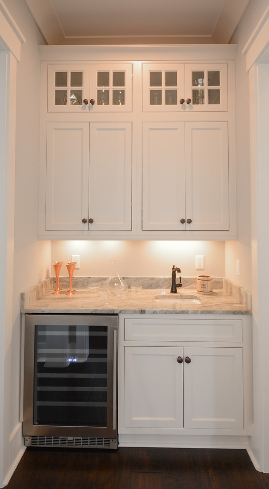 Klassisk inredning av en liten linjär hemmabar med vask, med en undermonterad diskho, skåp i shakerstil, vita skåp, marmorbänkskiva och brunt golv