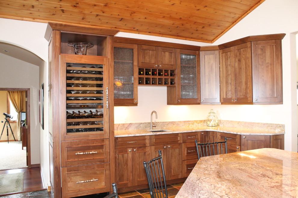 This is an example of an expansive traditional l-shaped wet bar in Denver with a submerged sink, flat-panel cabinets, dark wood cabinets, granite worktops, beige splashback and slate flooring.