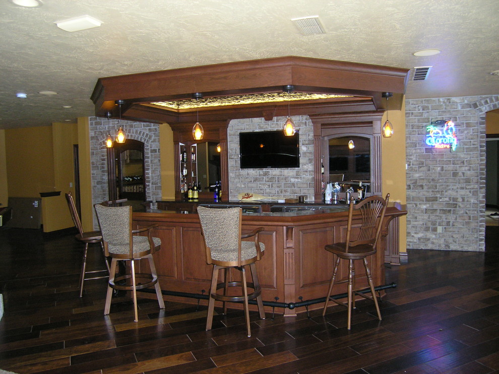 Cette photo montre un grand bar de salon linéaire chic en bois brun avec une crédence grise, une crédence en brique, parquet foncé, un sol marron, des tabourets, un placard avec porte à panneau surélevé et un plan de travail en granite.