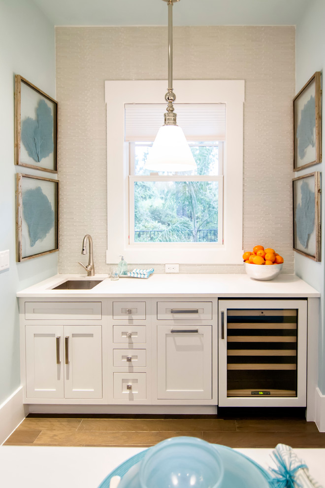 Example of a huge island style light wood floor and brown floor home bar design in Jacksonville with an undermount sink, white cabinets, granite countertops, white backsplash and recessed-panel cabinets