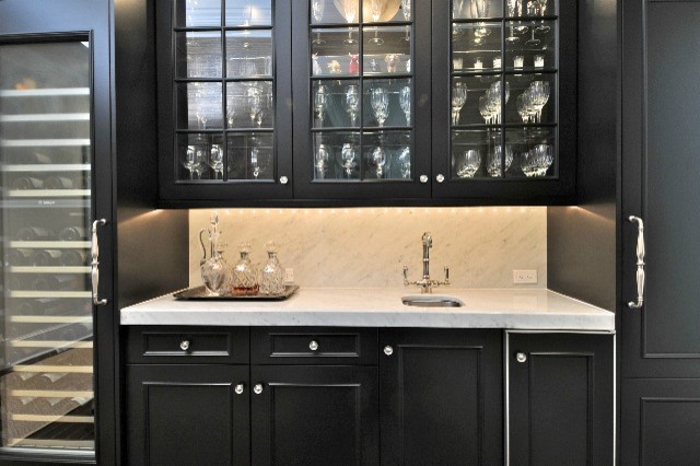 This is an example of a small traditional single-wall wet bar in Tampa with a submerged sink, glass-front cabinets, black cabinets, marble worktops, white splashback, marble splashback, medium hardwood flooring and brown floors.