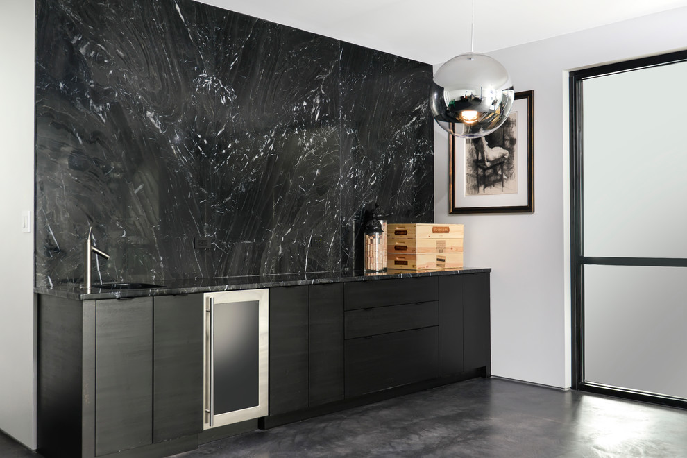 Esempio di un angolo bar con lavandino minimalista con ante nere, top in granito, paraspruzzi nero, paraspruzzi in marmo, pavimento in cemento e pavimento grigio