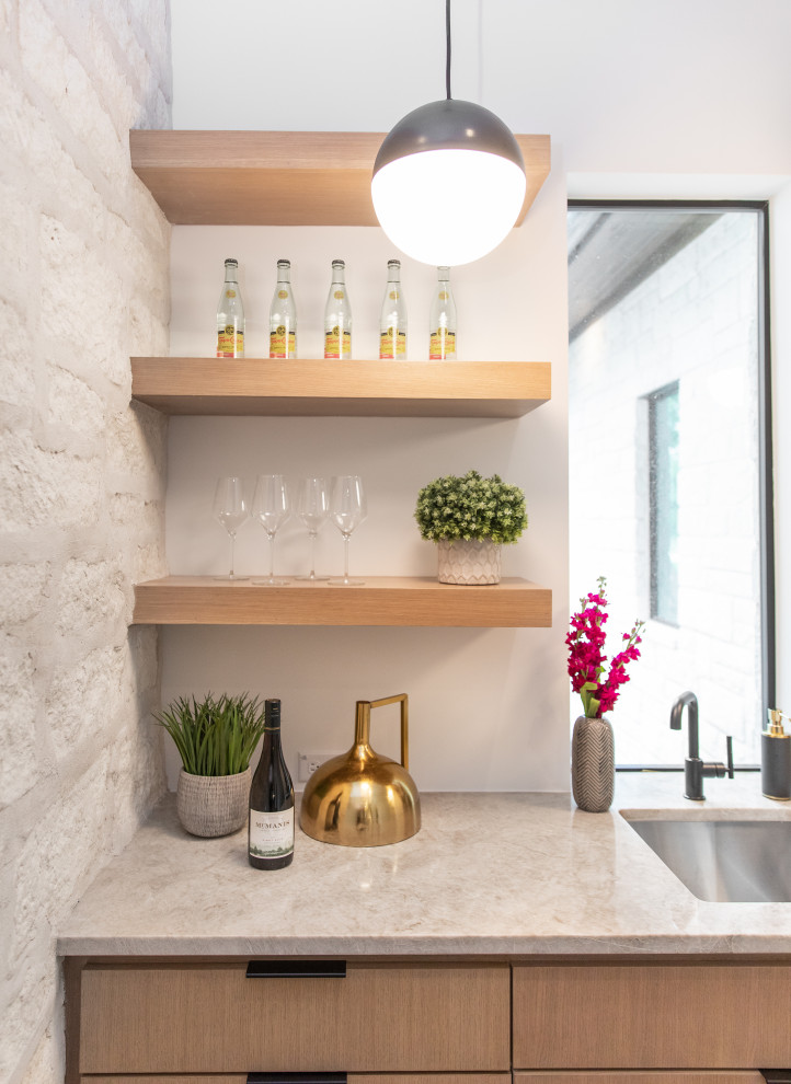 Immagine di un angolo bar con lavandino minimalista di medie dimensioni con lavello da incasso, ante in legno chiaro, top in granito e top beige