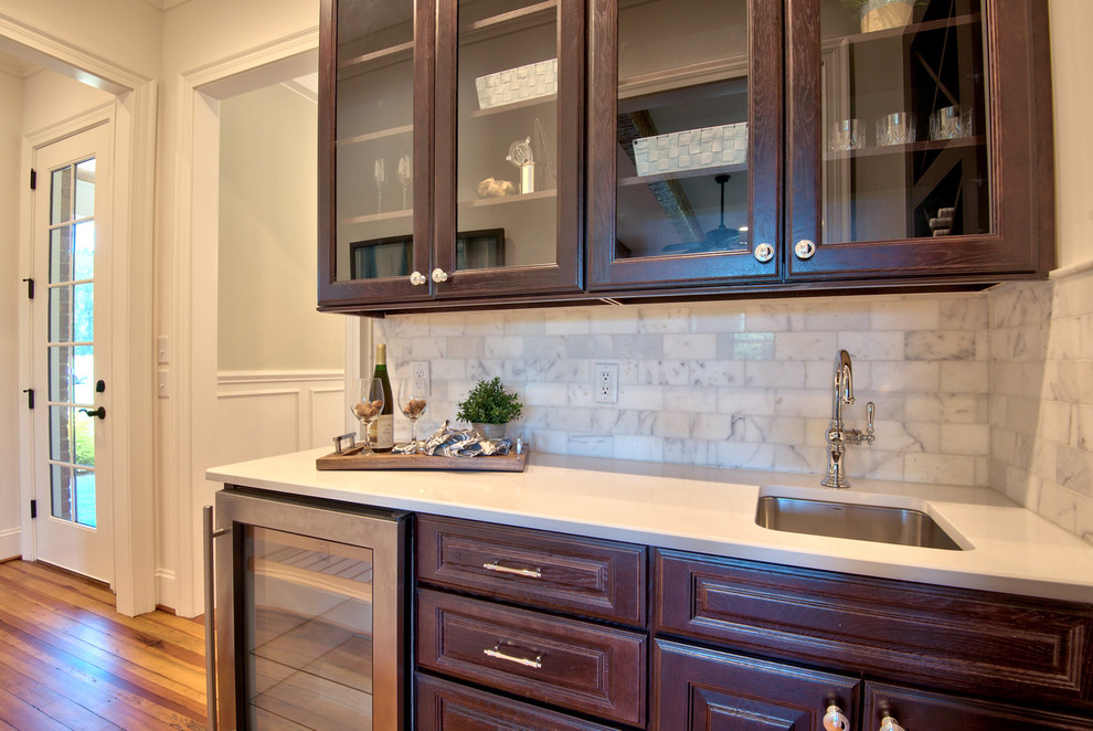 Example of a mid-sized country single-wall medium tone wood floor wet bar design in Raleigh with raised-panel cabinets, dark wood cabinets, quartz countertops and marble backsplash