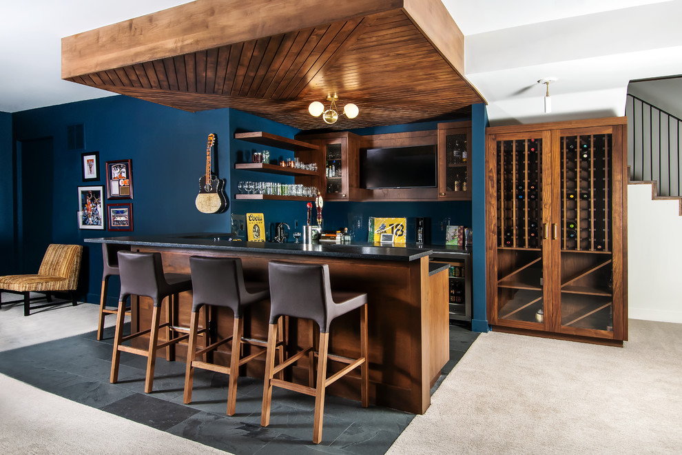 Ejemplo de bar en casa con barra de bar retro con armarios tipo vitrina, puertas de armario de madera en tonos medios, salpicadero azul, suelo gris y encimeras negras