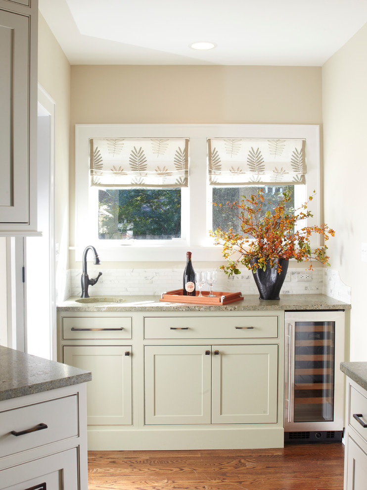 Exempel på en klassisk linjär hemmabar med vask, med en undermonterad diskho, luckor med profilerade fronter, gröna skåp, vitt stänkskydd och mellanmörkt trägolv