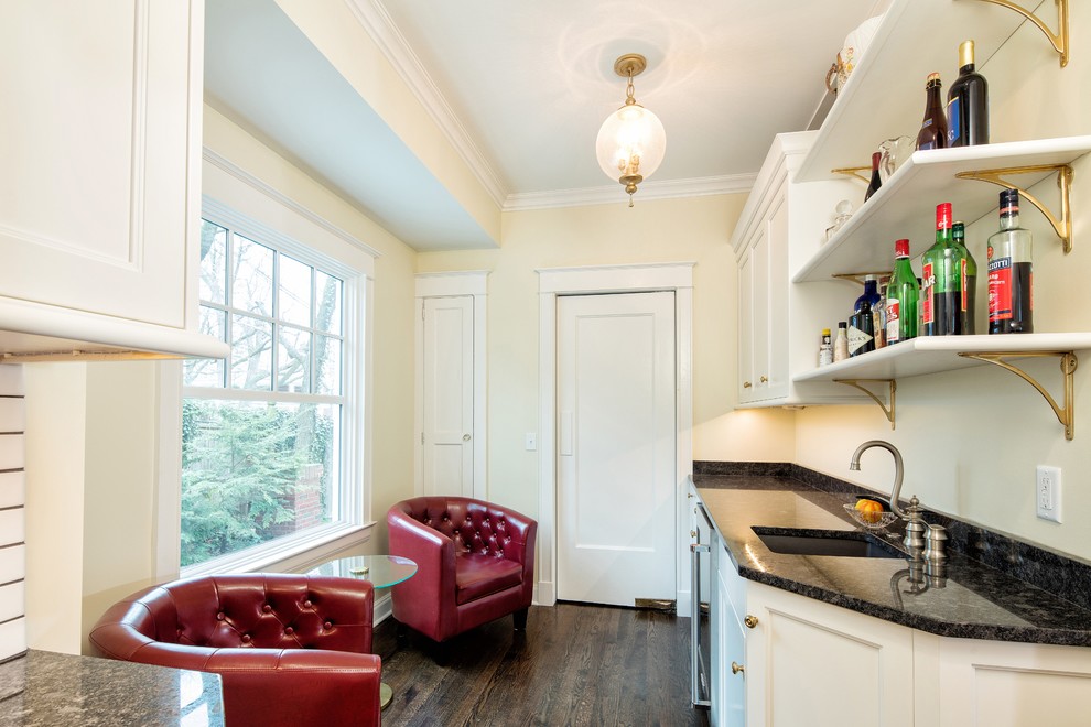 Klassische Hausbar in L-Form mit Unterbauwaschbecken, weißen Schränken, Granit-Arbeitsplatte, Küchenrückwand in Weiß, Rückwand aus Keramikfliesen und dunklem Holzboden in Kansas City