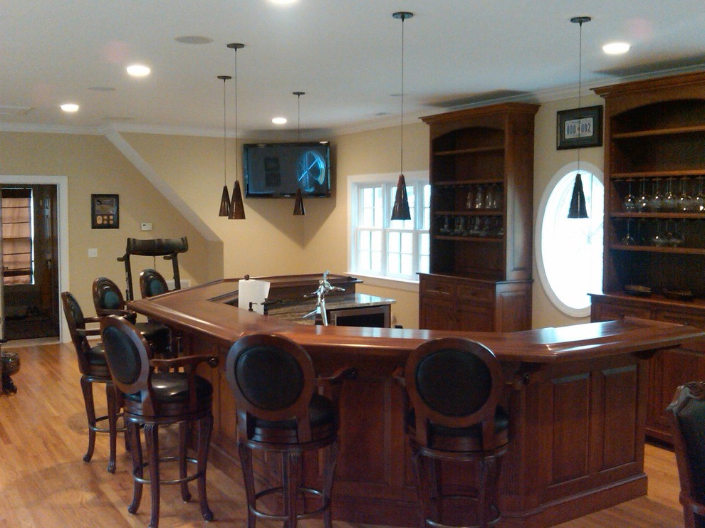 Cette image montre un grand bar de salon avec évier craftsman en U et bois foncé avec un évier posé, un placard sans porte, un plan de travail en bois, une crédence marron, parquet clair et un sol marron.
