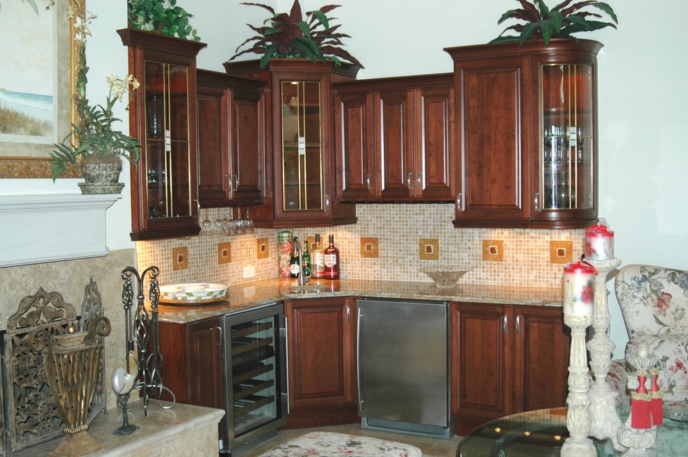 Example of a mid-sized classic l-shaped travertine floor and beige floor wet bar design in Other with an undermount sink, raised-panel cabinets, dark wood cabinets, granite countertops, beige backsplash, mosaic tile backsplash and beige countertops