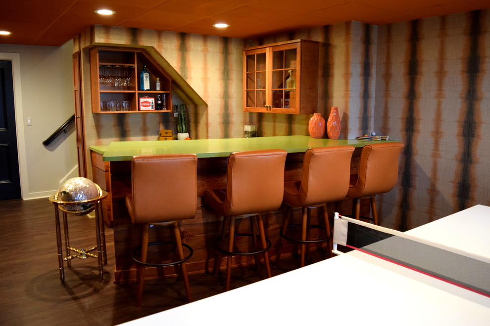 Modelo de bar en casa con barra de bar minimalista de tamaño medio con armarios con paneles empotrados, puertas de armario de madera oscura, encimera de acrílico y suelo de madera oscura