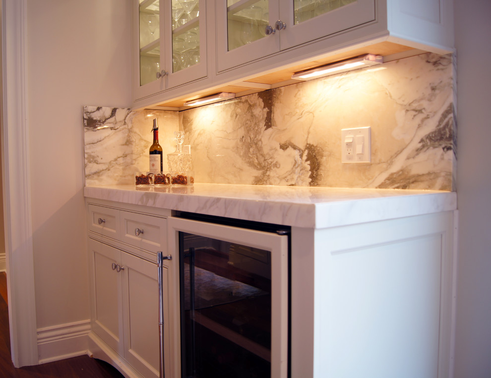 Photo of a small traditional single-wall wet bar in New York with no sink, shaker cabinets, white cabinets, engineered stone countertops, beige splashback, marble splashback, medium hardwood flooring and multi-coloured floors.