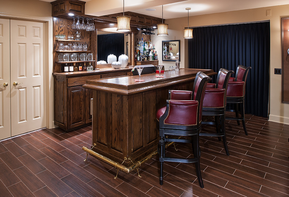 Cette image montre un bar de salon linéaire traditionnel en bois foncé de taille moyenne avec des tabourets, un placard avec porte à panneau surélevé, un plan de travail en bois, une crédence marron, une crédence en bois, un sol en vinyl et un sol marron.