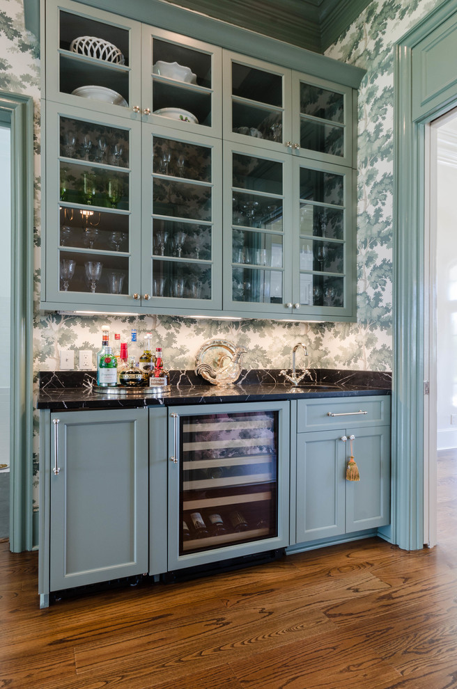 Inspiration för mellanstora klassiska linjära hemmabarer med vask, med en undermonterad diskho, gröna skåp, marmorbänkskiva, svart stänkskydd, mörkt trägolv och luckor med infälld panel