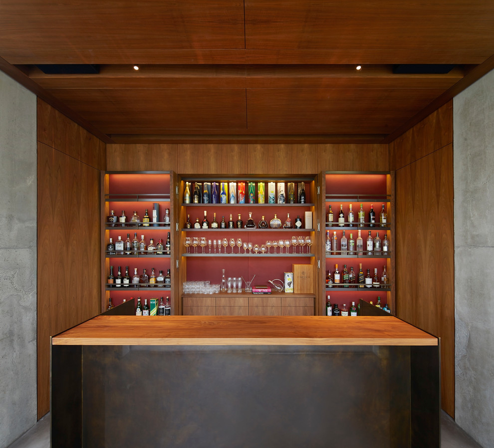 Idee per un ampio angolo bar con lavandino minimal con ante lisce, ante in legno bruno, top in legno, paraspruzzi rosso, pavimento in cemento e pavimento grigio