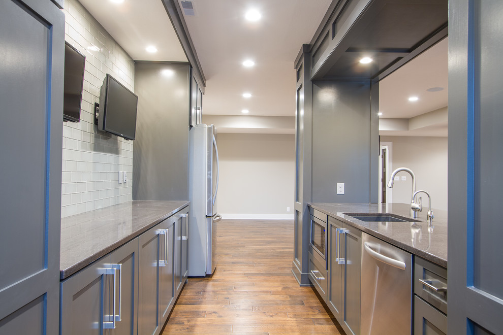 This is an example of a medium sized traditional galley breakfast bar in Omaha with a submerged sink, shaker cabinets, grey cabinets, white splashback, glass tiled splashback and dark hardwood flooring.