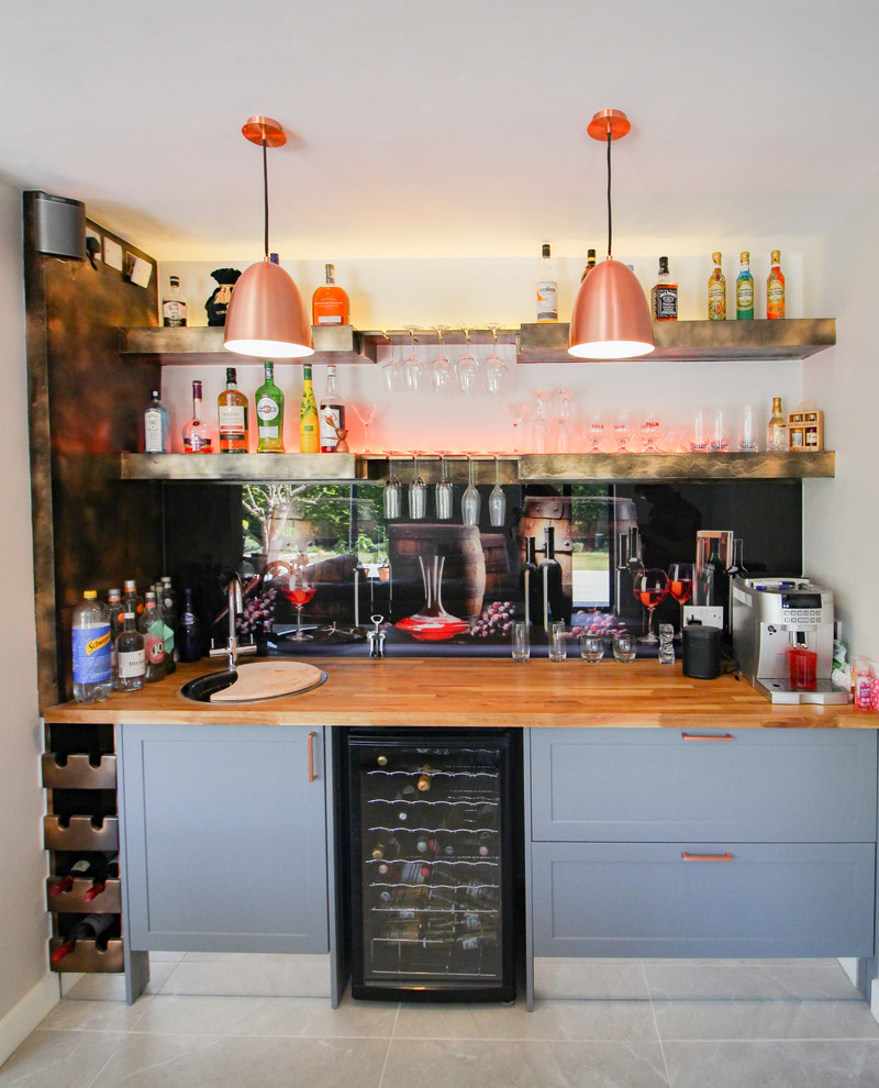 Photo of an expansive classic single-wall wet bar in London with shaker cabinets, grey cabinets, wood worktops, ceramic flooring, grey floors, black splashback, glass sheet splashback, beige worktops and a built-in sink.