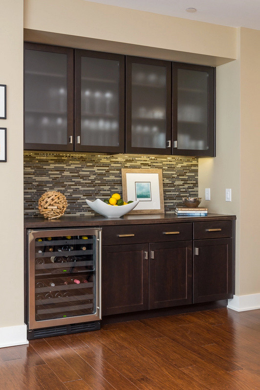 Photo of a contemporary single-wall wet bar in Indianapolis with glass-front cabinets, dark wood cabinets, multi-coloured splashback, glass tiled splashback and dark hardwood flooring.