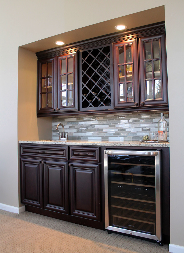 Example of a small transitional single-wall carpeted wet bar design in Detroit with an undermount sink, raised-panel cabinets, dark wood cabinets, granite countertops, beige backsplash and glass tile backsplash