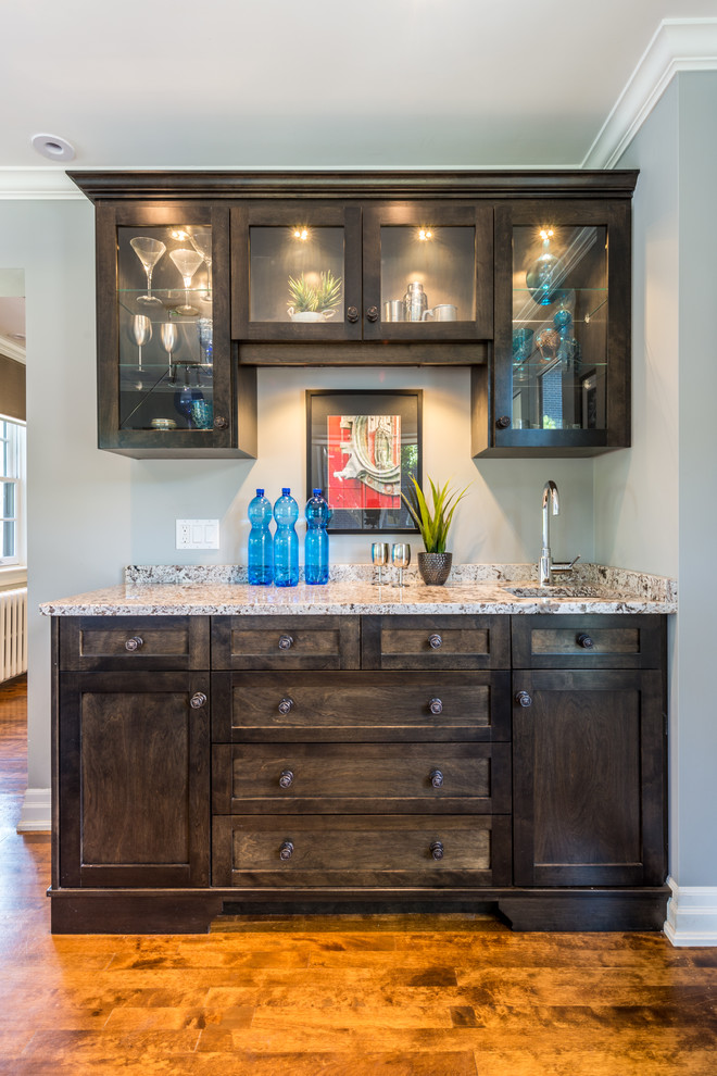 This is an example of a small rustic single-wall wet bar in Ottawa with a submerged sink, glass-front cabinets, dark wood cabinets, granite worktops, medium hardwood flooring, brown floors and grey worktops.