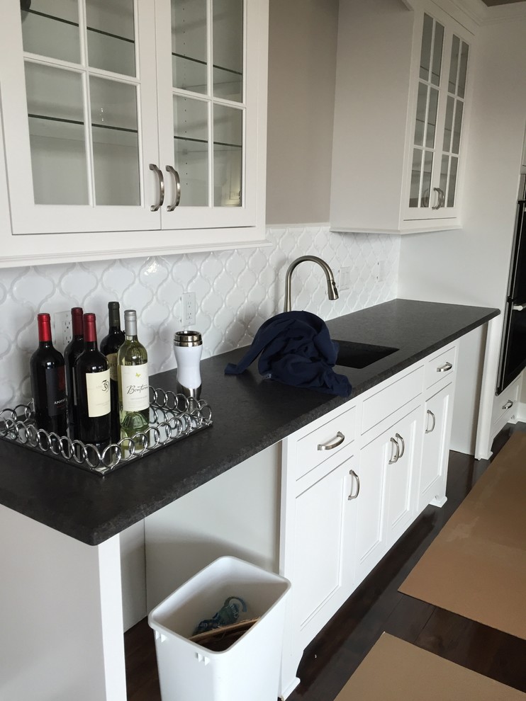 Example of a mid-sized transitional u-shaped home bar design in Milwaukee with beaded inset cabinets, white cabinets, granite countertops, white backsplash, ceramic backsplash and an undermount sink