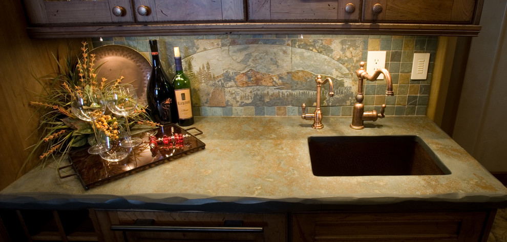 Small mountain style galley seated home bar photo in Denver with an undermount sink, raised-panel cabinets, medium tone wood cabinets, beige backsplash and slate backsplash