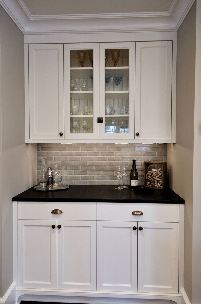 Exempel på en liten klassisk svarta linjär svart hemmabar med vask, med luckor med infälld panel, vita skåp, bänkskiva i kvarts, beige stänkskydd, stänkskydd i glaskakel, brunt golv och mellanmörkt trägolv