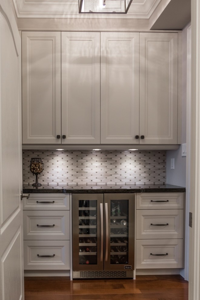 Inspiration for a mid-sized transitional single-wall medium tone wood floor home bar remodel in Toronto with shaker cabinets, granite countertops, mosaic tile backsplash, gray backsplash, white cabinets and no sink
