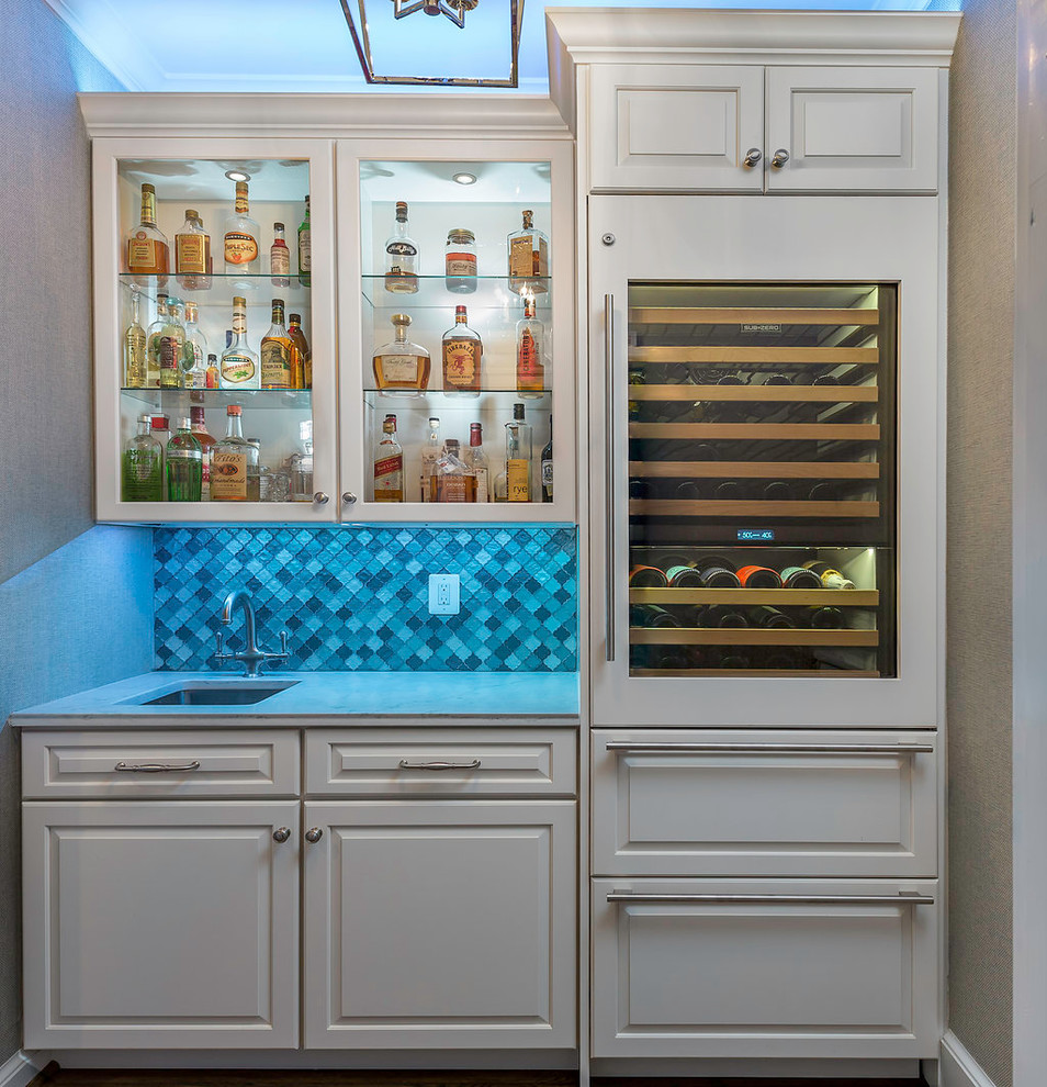 Klassisk inredning av en liten vita vitt hemmabar med vask, med en undermonterad diskho, luckor med upphöjd panel, vita skåp, bänkskiva i kvarts, blått stänkskydd, stänkskydd i glaskakel, mellanmörkt trägolv och brunt golv