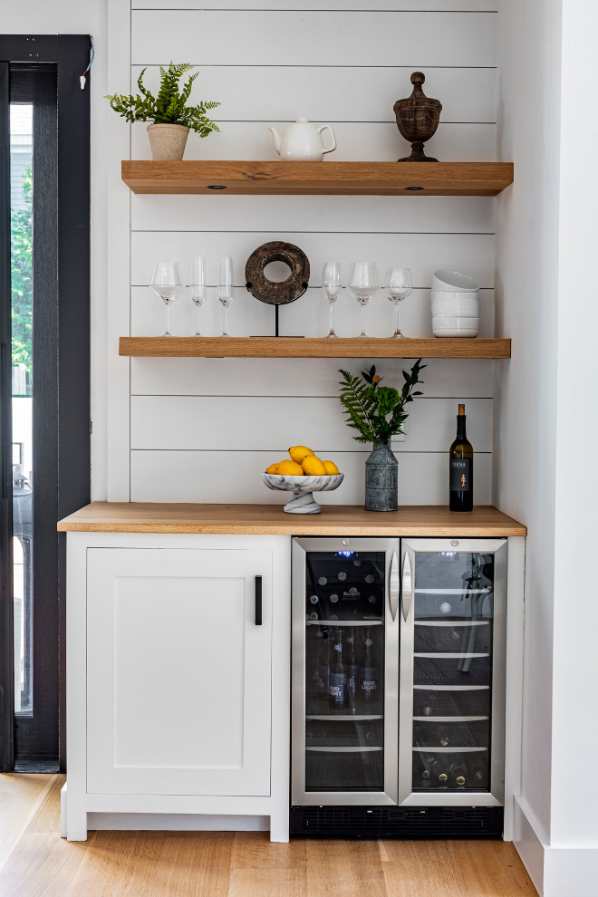 This is an example of a small traditional single-wall home bar in Boston with no sink, shaker cabinets, white cabinets, wood worktops, white splashback, wood splashback, light hardwood flooring, beige floors and beige worktops.