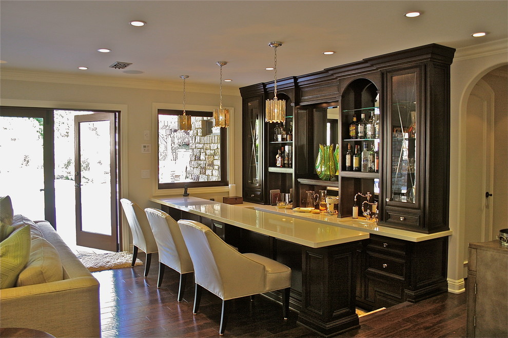 This is an example of a medium sized classic galley breakfast bar in Orange County with a submerged sink, glass-front cabinets, dark wood cabinets, composite countertops, mirror splashback and dark hardwood flooring.