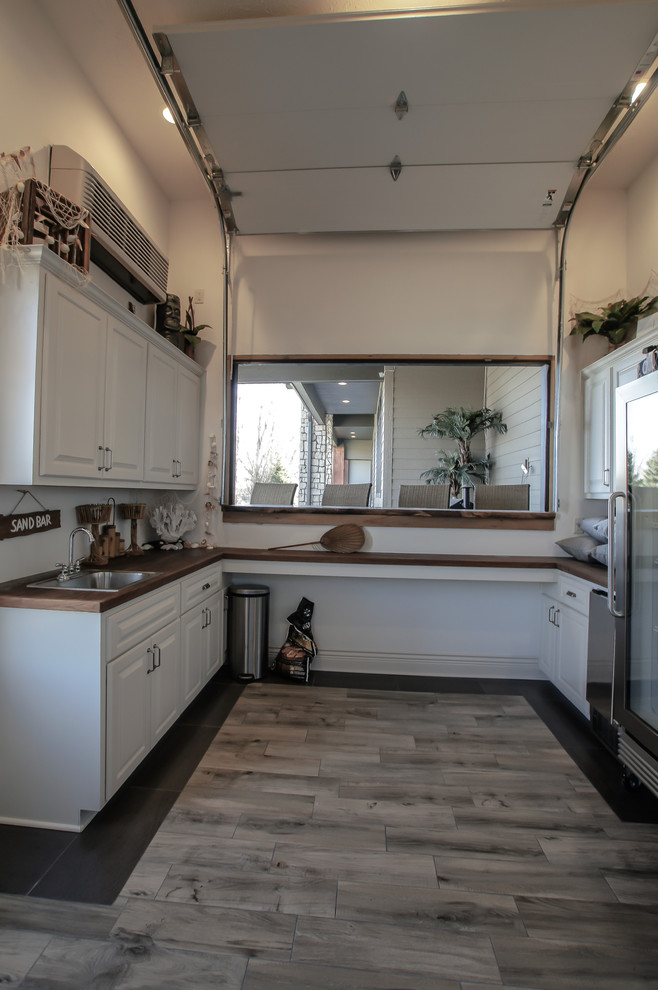 This is an example of a coastal single-wall wet bar in Omaha with raised-panel cabinets, white cabinets, wood worktops, ceramic flooring, grey floors and brown worktops.