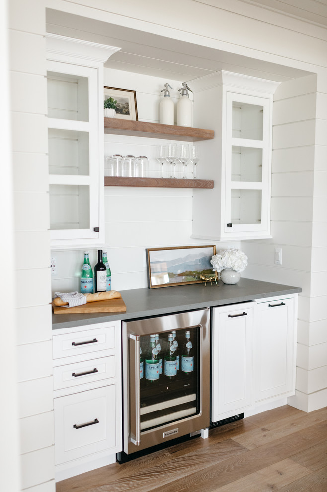 Inspiration for a mid-sized farmhouse single-wall medium tone wood floor and brown floor wet bar remodel in Detroit with no sink, shaker cabinets, white cabinets, quartz countertops, white backsplash, wood backsplash and gray countertops