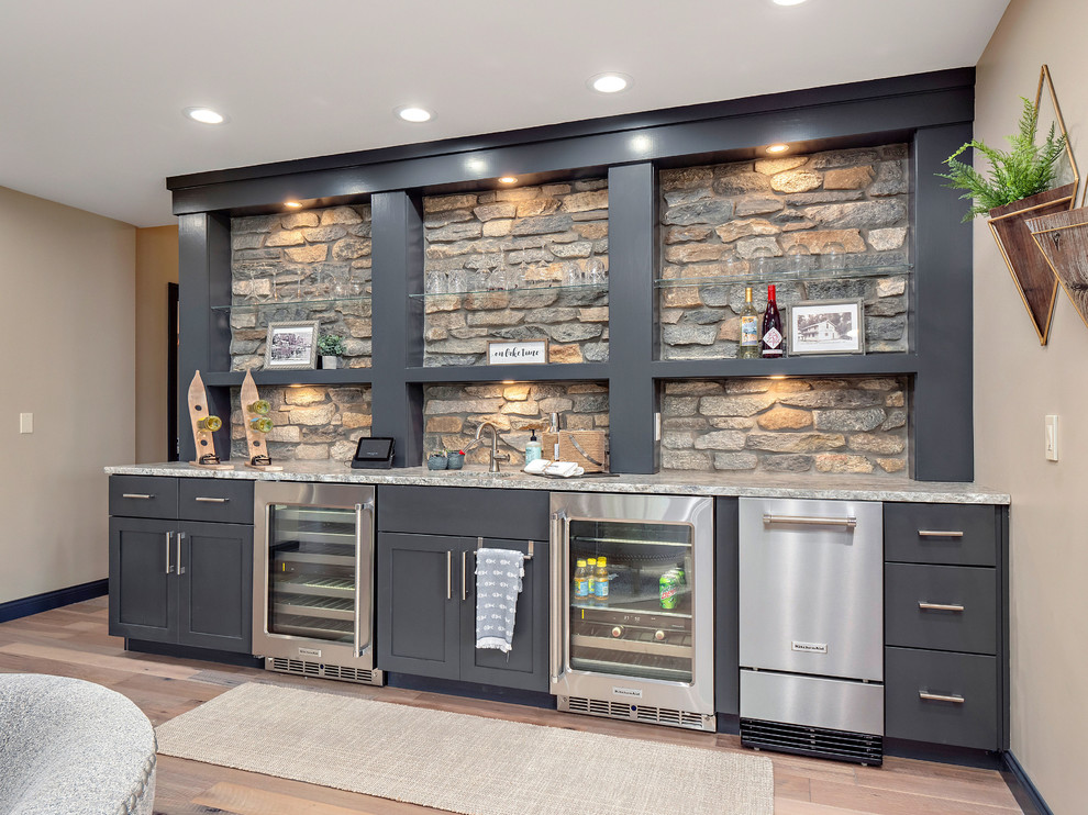 Inspiration for a rustic single-wall medium tone wood floor and brown floor wet bar remodel in Other with an undermount sink, flat-panel cabinets, gray cabinets, gray backsplash, stone tile backsplash and gray countertops