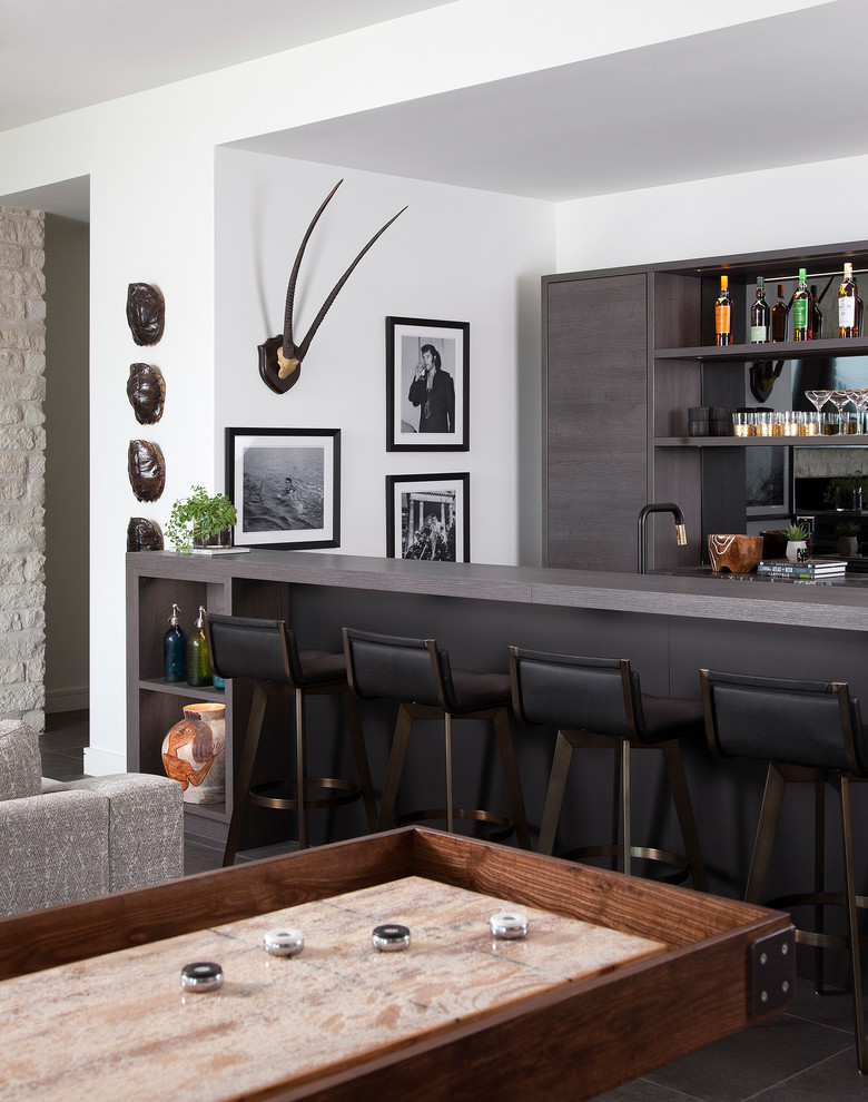 Aménagement d'un bar de salon parallèle contemporain en bois foncé avec des tabourets, un placard à porte plane, une crédence miroir, un sol marron et un plan de travail gris.